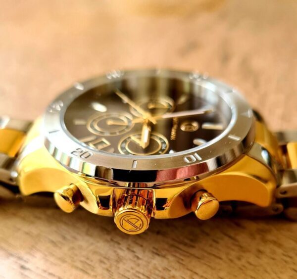 A gold and silver watch sitting on top of a wooden table.