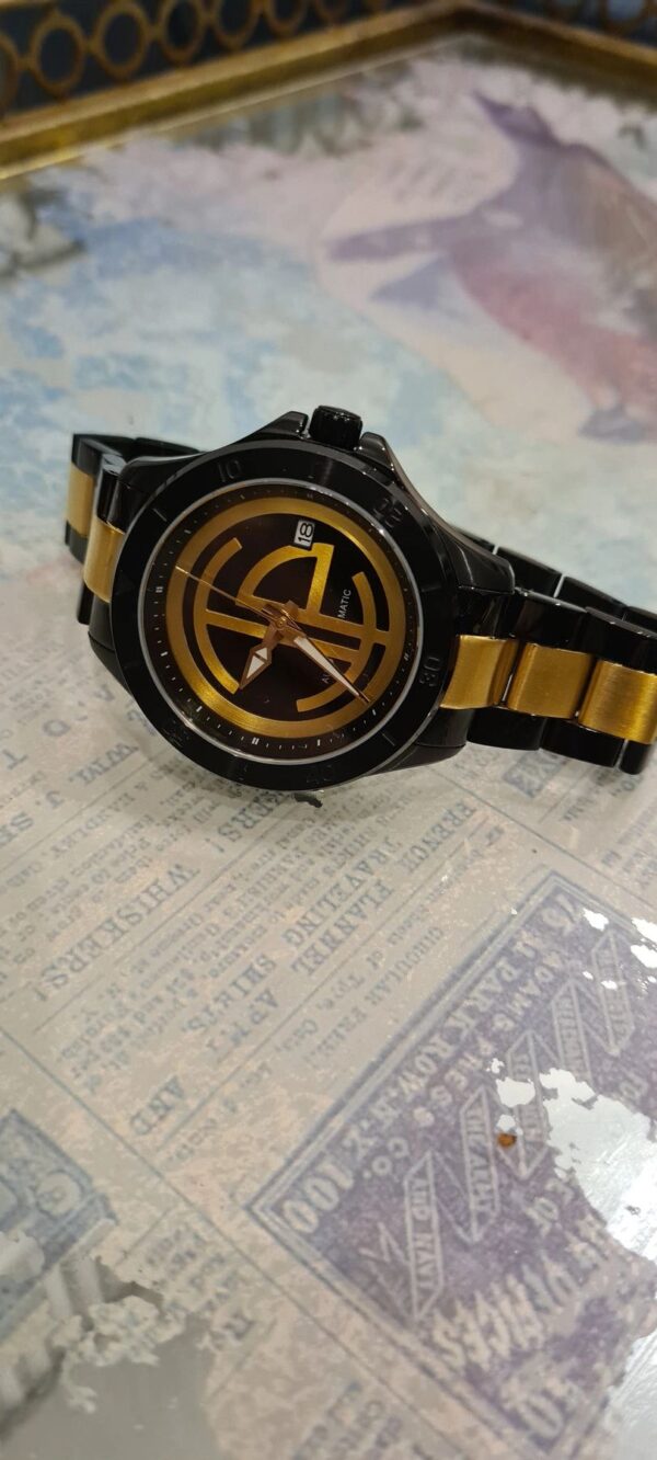 A black and gold watch sitting on top of a newspaper.
