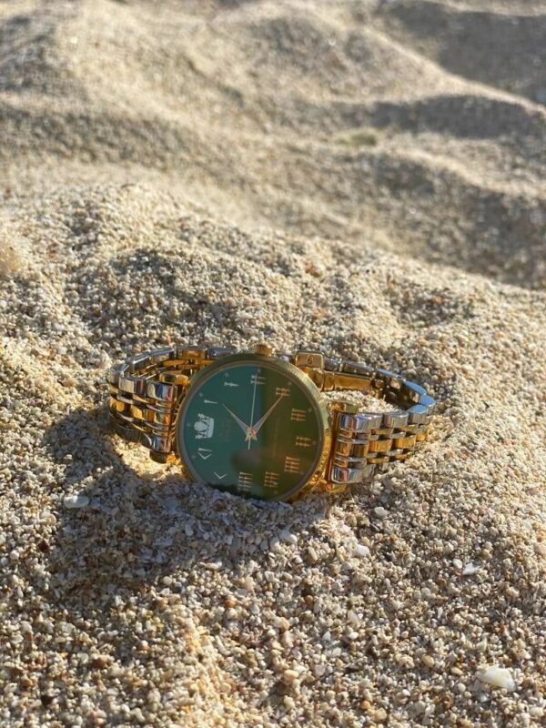 A watch is laying in the sand on the beach.