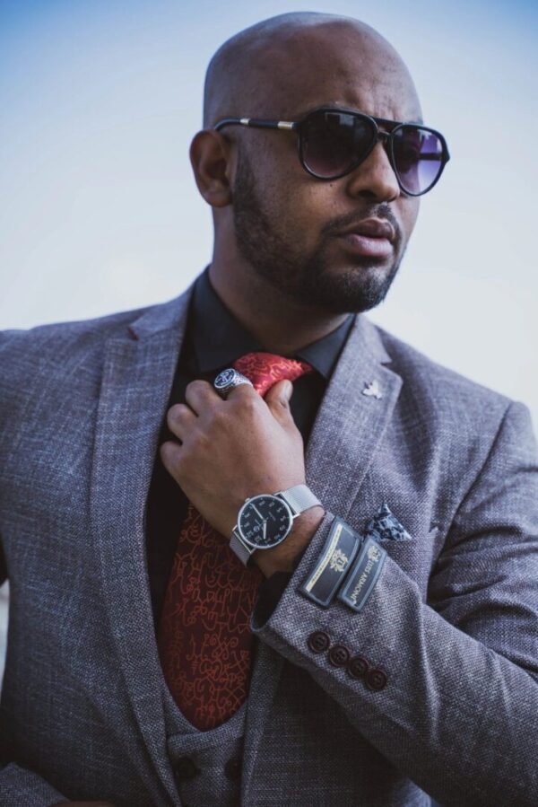 A man in sunglasses and a suit adjusting his tie.