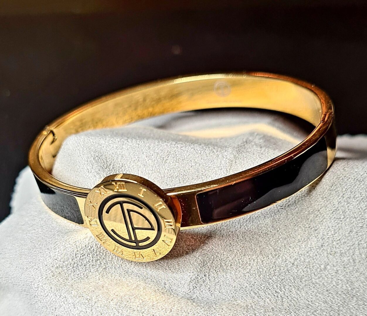 A gold and black bracelet sitting on top of a white cloth.