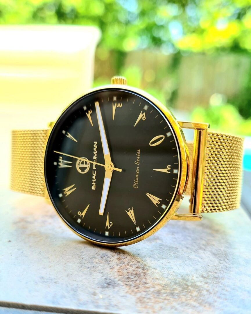 A gold watch with black face sitting on top of a table.