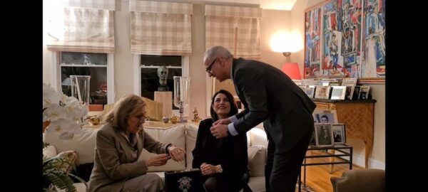 A man in suit and glasses handing something to two women.