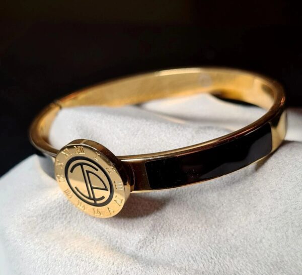 A gold bracelet with a black band and a round logo.